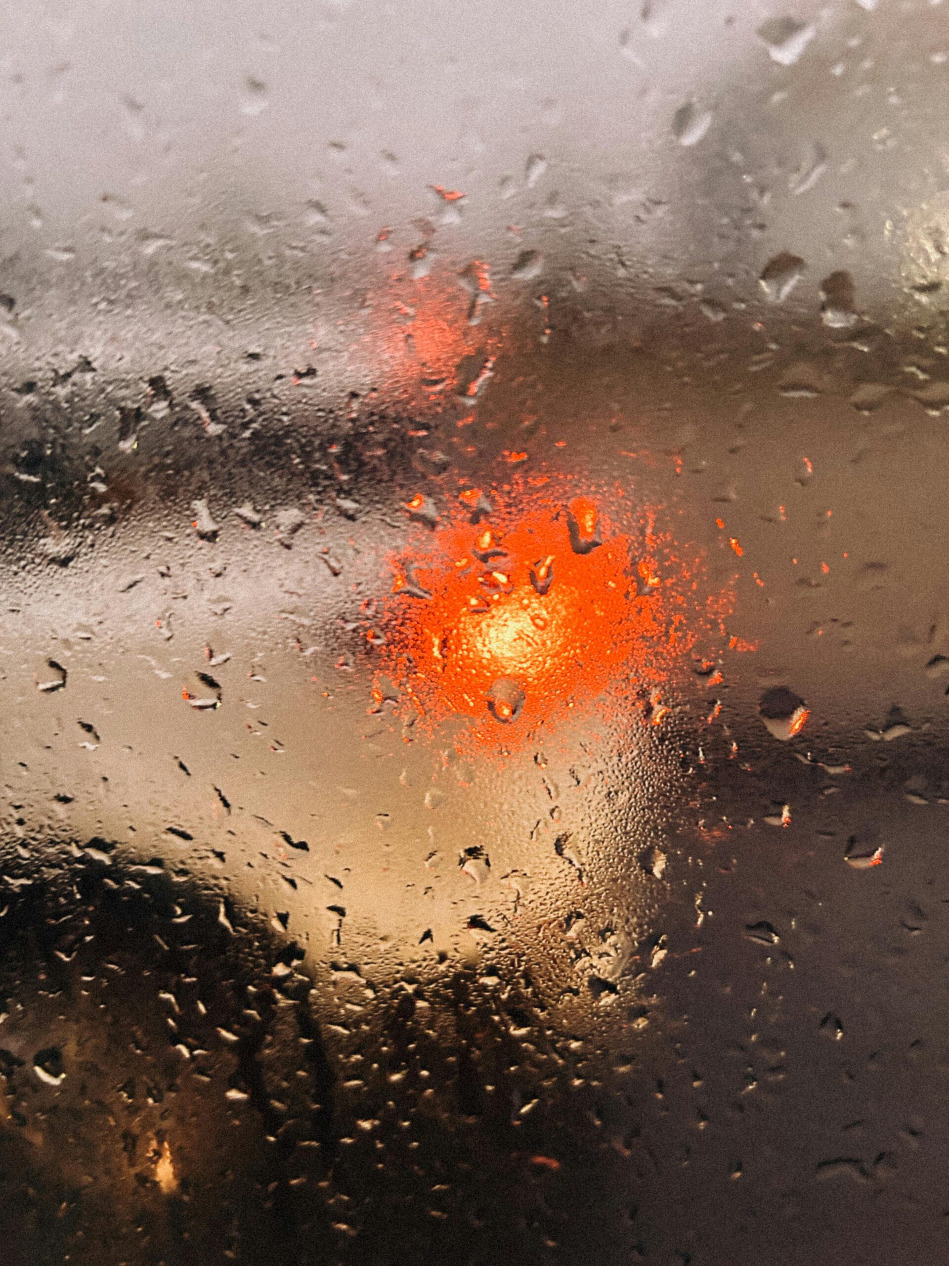 Blurred view through raindrop-covered glass showcasing vibrant traffic light.